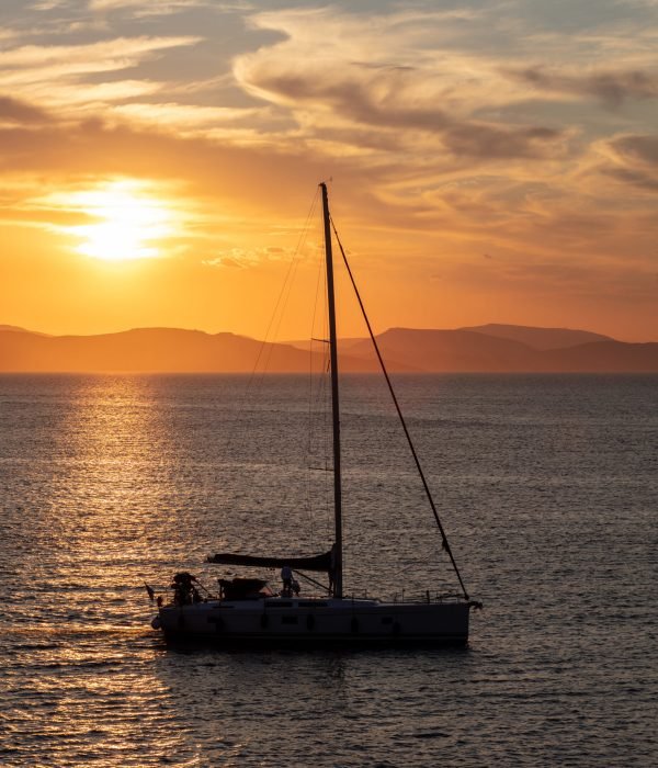 Sailing at sunset in the Aegean sea, Greece. Sailboat on calm sea and orange sky background,